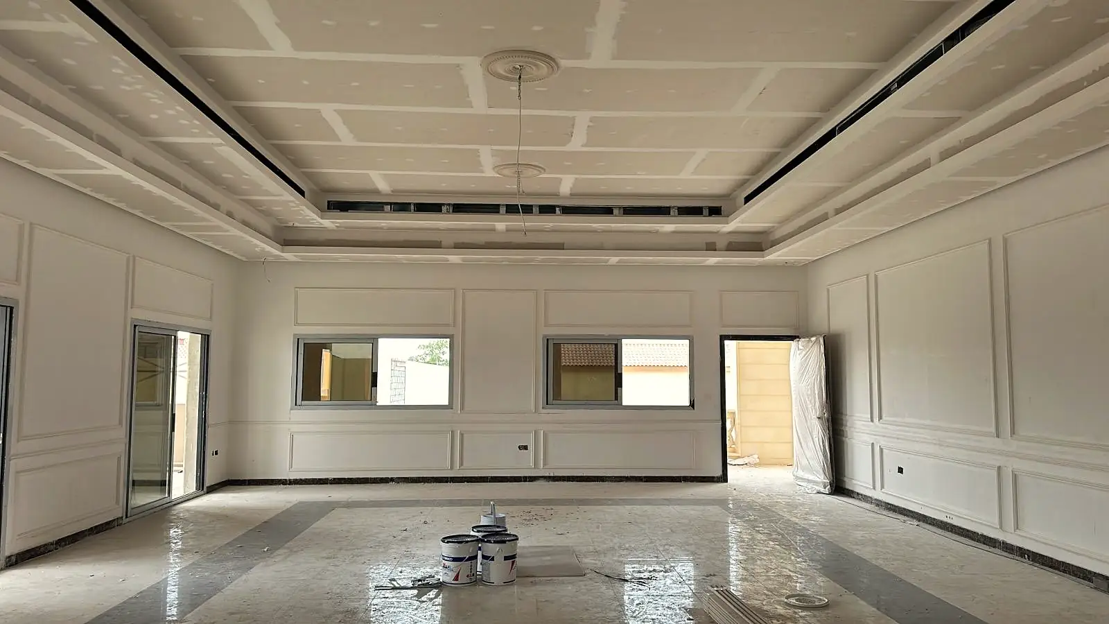 Large hall with a new gypsum ceiling, cove lines and wall mouldings, paint tins on the floor