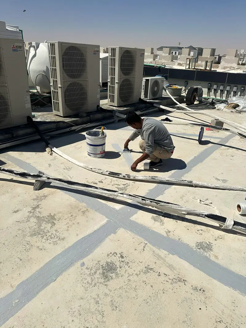 Worker sealing roof joints on a flat rooftop next to outdoor AC units
